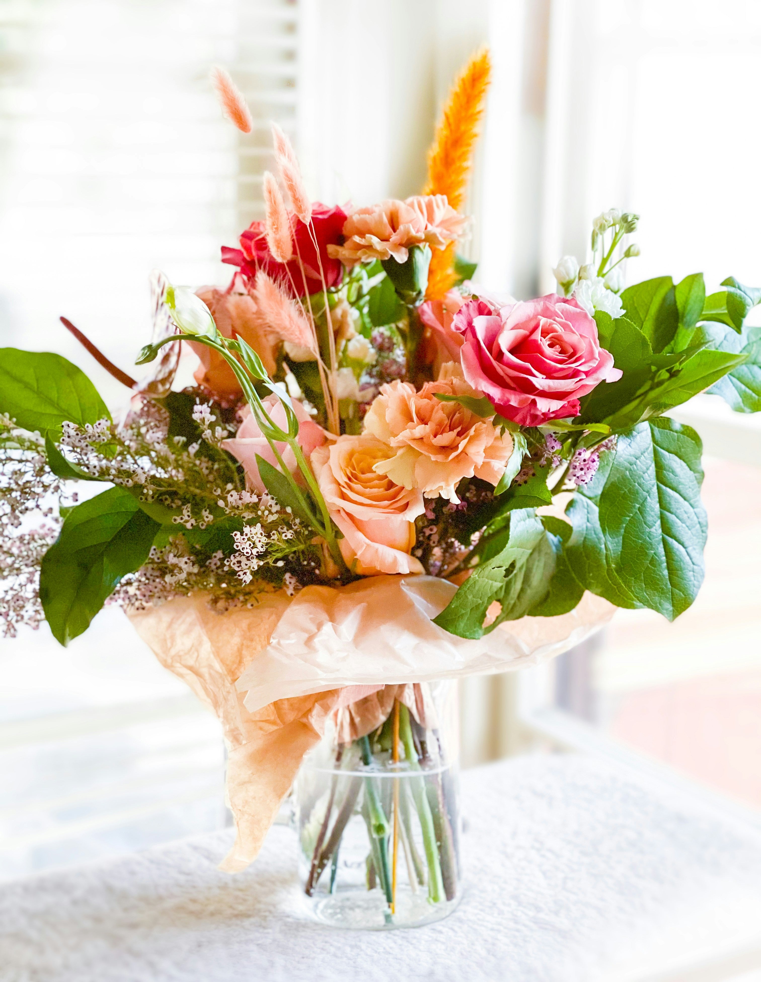 Bouquet of flowers with pink and orange roses in a clear vase on a white surface.